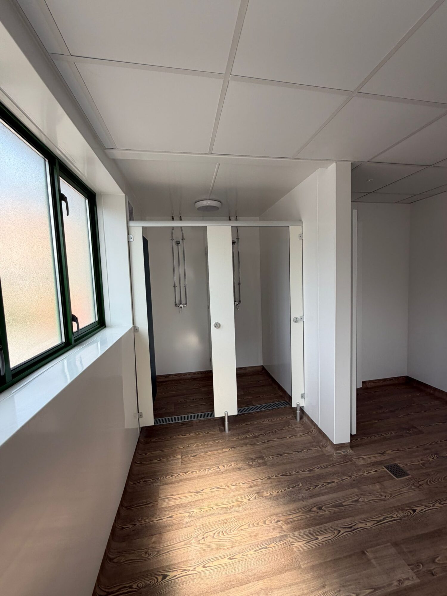 Refurbished changing facilities with white cubicles and wood-effect flooring at Wimbledon Park Sports Centre, Southsea